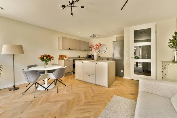 Odanın ortasında ahşap döşemeli ve beyaz mobilyalı bir oturma odası açık bir mutfak alanıdır.