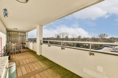 Ahşap döşemeleri ve beyaz duvarları olan bir balkon, bir apartmandan şehir manzarasına bakıyor.