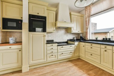 Dolabın önündeki adada beyaz dolapları ve siyah tezgahları olan bir mutfak. Büyük bir pencere var.