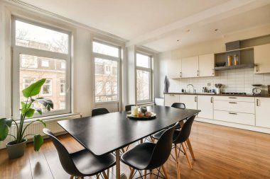 Büyük pencereli bir odada, şehir manzarasına bakan bir yemek masası ve sandalyeler.