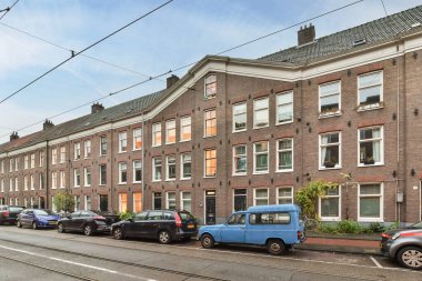 Amsterdam, Hollanda - 10 Nisan 2021: Yolun kenarına park edilmiş bazı arabalar birçok penceresi olan tuğla apartmanların önüne park edilmiş.