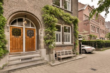 Ön kapısında yeşil sarmaşıklar olan tuğladan bir ev ve beyaz bir arabaya giden bir girişe çıkan merdivenler.