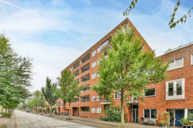Amsterdam, Hollanda - 10 Nisan 2021: Önünde ağaçlar olan bir apartman ve caddelerde yan yana duran binalar.