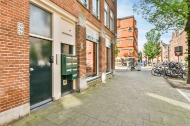 Amsterdam, Hollanda - 10 Nisan 2021: Yolun kenarına bisikletlerle park edilmiş bir şehir caddesi ve uzaktaki tuğlalı binalar kırmızı tuğladan duvarlardır