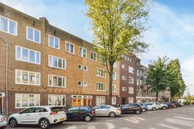 Amsterdam, Hollanda - 10 Nisan 2021: Birçok penceresi olan tuğladan apartmanların önüne park edilmiş bazı arabalar