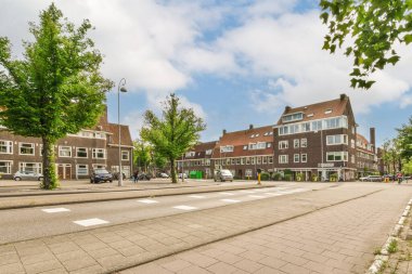 Amsterdam, Hollanda - 10 Nisan 2021: Kenarında arabalar, arka tarafında binalar olan bir şehir caddesi, bazı insanlar yolda yürüyor