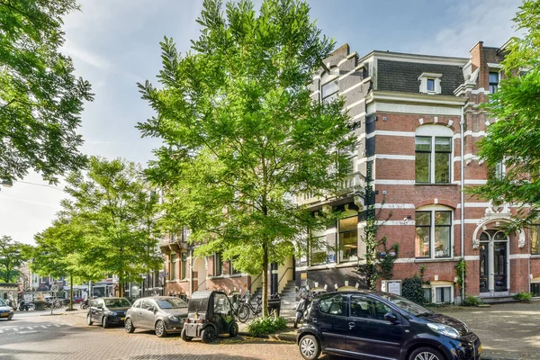 2021年4月10日 荷兰阿姆斯特丹 一条城市街道 路边停着汽车 道路两旁的建筑物前生长着蓝天下的树木 — 图库照片