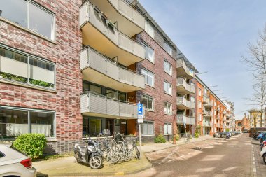 Önünde bisikletleri olan bir apartman dairesi ve cadde boyunca park etmiş arabalar.