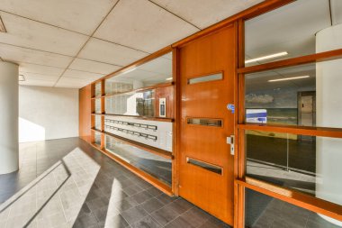 Her iki tarafında ahşap ve cam kapılar olan modern bir bina. Pencere camlarında güneş ışığı var.