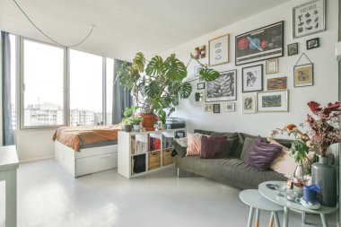 Amsterdam, Hollanda - 10 Nisan 2021: Odadaki kanepenin üstündeki duvarda bir sürü bitki ve resim olan bir oturma odası çok beyaz.