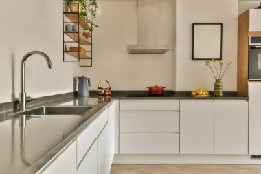 Görüntünün ortasında beyaz dolapları ve siyah tezgahları olan modern bir mutfak bir fırın, bulaşık makinesi ve lavabo.