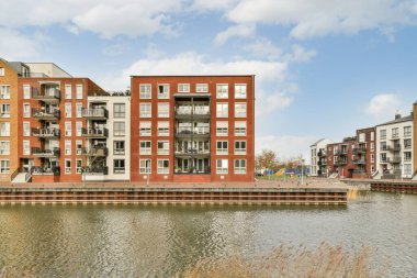 Amsterdam, Hollanda - 10 Nisan 2021: Sudaki bazı binalar mavi gökyüzü ve beyaz bulutlar ile gölün karşısından çekilmiştir.