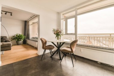 İki sandalyeli bir oturma odası ve büyük bir pencerenin önünde bir masa. Dışarıdaki şehre bakıyor.