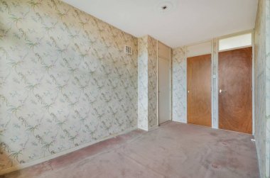 Duvarlarında çiçek kağıtları olan boş bir oda ve başka bir odaya açılan ahşap kapı.