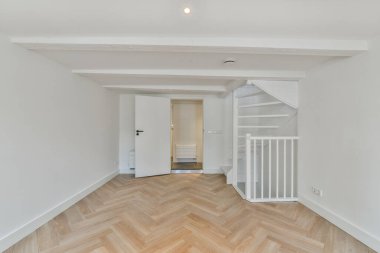 Beyaz duvarları ve ahşap döşemeleri olan boş bir oda. İkinci kata çıkan bir merdiven var.