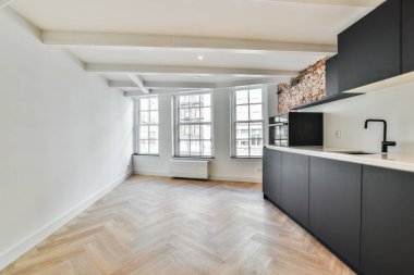 Ahşap döşemeleri ve beyaz duvarları olan boş bir mutfak. Ahşap zeminleri, siyah dolapları ve geniş pencereleri olan bir oda.