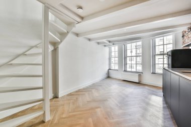 Ahşap döşemeleri ve beyaz duvarları olan boş bir oda. Bu dairenin ikinci katına çıkan merdivenler.