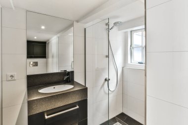 Duvarlarında siyah beyaz fayanslar olan modern bir banyo, lavabo, ayna ve duş kabini.