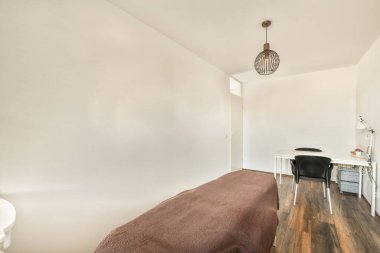 Yatağı, masası ve lambası olan bir yatak odası yatağın önünde beyaz boyalı duvarlar var.