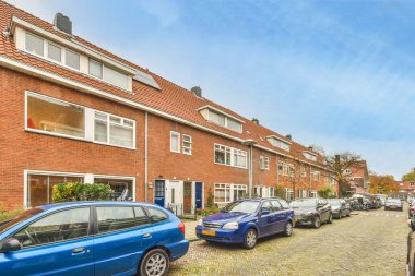 Bazı arabalar tuğlalı bir caddenin kenarına park edilmiş kırmızı tuğlalı evlerin önüne.