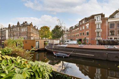 Amsterdam, Hollanda - 10 Nisan 2021: Kanalların diğer tarafından görüldüğü üzere, her iki tarafında binalar bulunan bazı evler ve tekneler