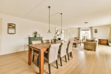 Odasında ahşap döşeme ve beyaz duvarlar olan bir yemek odası oturma odasından mutfak alanına alınır.