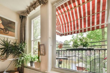Amsterdam, Netherlands - 10 April, 2021: a window with red and white stripes hanging on the windowsills in a living room filled with potted plants clipart