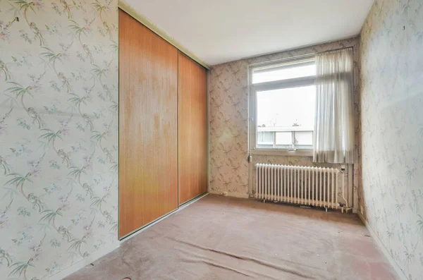 an empty room with floral wallpaper on the walls and wood paneled door to the left, theres a rad