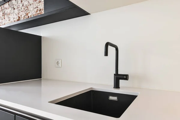 Stock image a black and white kitchen with brick wall in the back, sink is at the center of the room on the right hand side