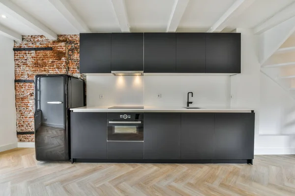 a kitchen with black cabinets and white counter tops on the island in front of the sink is an exposed brick wall