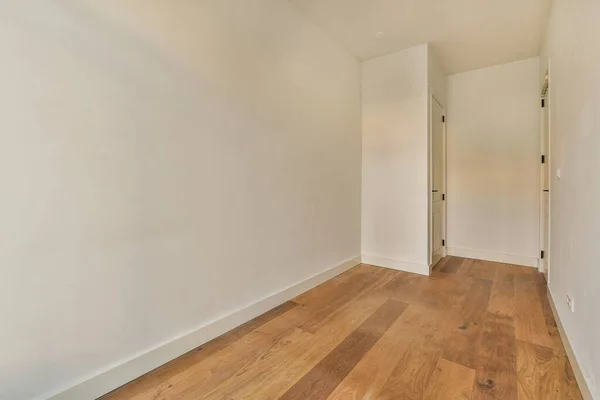右边是一个有白色墙壁和木制地板的空房间 有一扇门通往另一个房间 — 图库照片