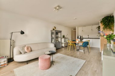 Beyaz duvarları ve ahşap döşemeleri olan bir oturma odası. Gri bir halının üzerine bej bir kanepe serilmiş.