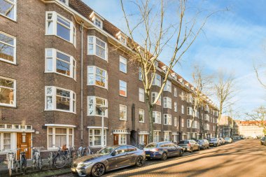 Amsterdam, Hollanda - 10 Nisan 2021: Bazı arabalar beyaz pencereli tuğla apartmanların önüne park etmiş.