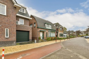 Arka planda evleri olan bir cadde ve evin yanına park edilmiş bir araba.