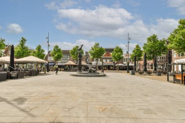 Fotoğrafın ortasında masaları, şemsiyeleri ve ağaçları olan bir açık hava alanı açık mavi gökyüzüdür.