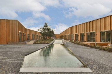 Ağaçlarla çevrili, ahşap duvarları ve tuğla geçitleri olan bir avlunun ortasında bir su kaynağı.