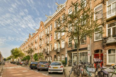 Amsterdam, Hollanda - 10 Nisan 2021: Birçok pencere ve bant olan bir apartmanın önünde caddenin kenarına parketmiş bisikletler