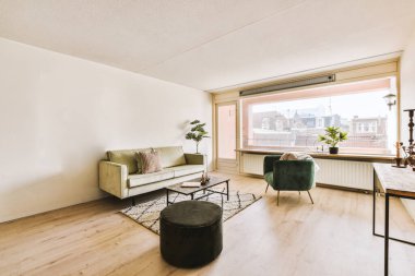 Odanın ortasında beyaz duvarları ve ahşap döşemeleri olan bir oturma odası, yeşil bir kanepe var.