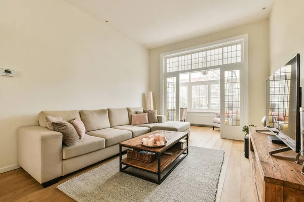 stock image a living room with a couch, coffee table and flat screen tv on the wall in front of the window