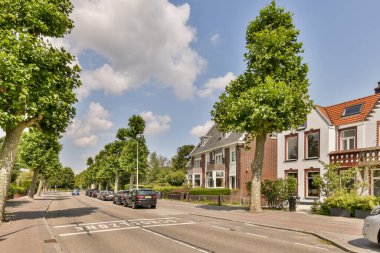 Amsterdam, Hollanda - 10 Nisan 2021: yan tarafında arabalar park edilmiş boş bir cadde ve her iki tarafında yol boyunca ağaçlar dizilmiş.