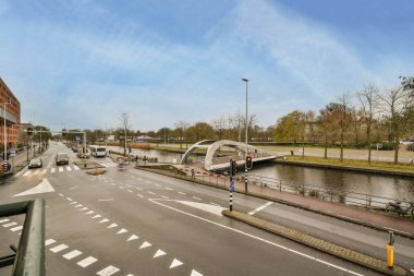 Amsterdam, Hollanda - 10 Nisan 2021: Yol üzerinde beyaz çizgiler ve nehir boyunca binalar bulunan kentsel bir bölgenin ortasındaki bir sokak