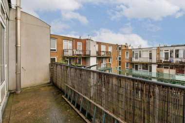 Güneşli bir günde bir balkondan görüldüğü gibi, arka planda bazı binalar ve üzerinde mavi gökyüzü olan bir dış alan.