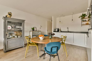 Beyaz duvarları, ahşap döşemeleri ve mavi sandalyelerle çevrili ahşap masası olan bir evde mutfak ve yemek odası.