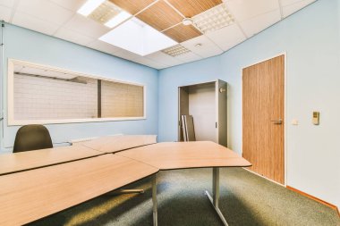 Odanın ortasında mavi duvarları ve hafif ahşap masaları olan boş bir ofis bir tavan penceresidir.