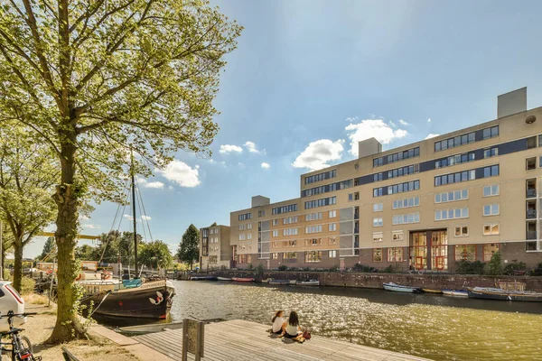 stock image Amsterdam, Netherlands - 10 April, 2021: a boat docked in the water next to a large building with many windows and bals on its sides