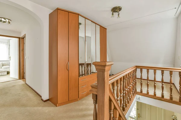 a room with wooden furniture and white walls, including a staircase leading up to the second floor there is a mirror on the wall