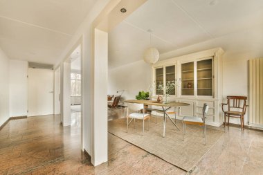 Ahşap döşemeli, beyaz duvarlı ve oturma odasının kapısı açık bir evde mutfak ve yemek odası.