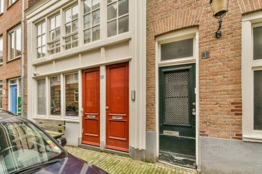 Amsterdam, Hollanda - 10 Nisan 2021: Tuğla bir binanın önüne park edilmiş kırmızı kapılı ve pencereli bir araba