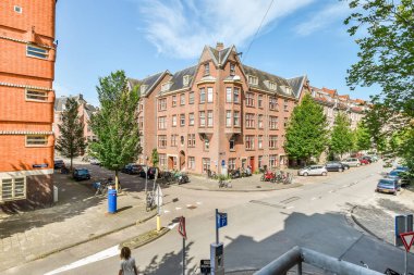 Amsterdam, Hollanda - 10 Nisan 2021: Kenarında arabalar park edilmiş ve insanlar binanın önünde sağda yürüyen bir şehir sokağı