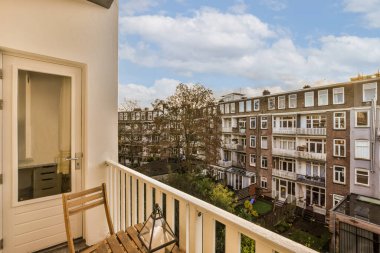 Arka planda binalar olan bir balkon ve sağ tarafta sokağa bakan ahşap bir bank.